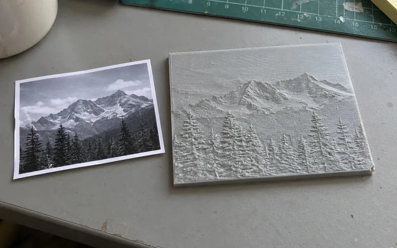 Gray mountain and pine tree relief plaque beside its source photograph.