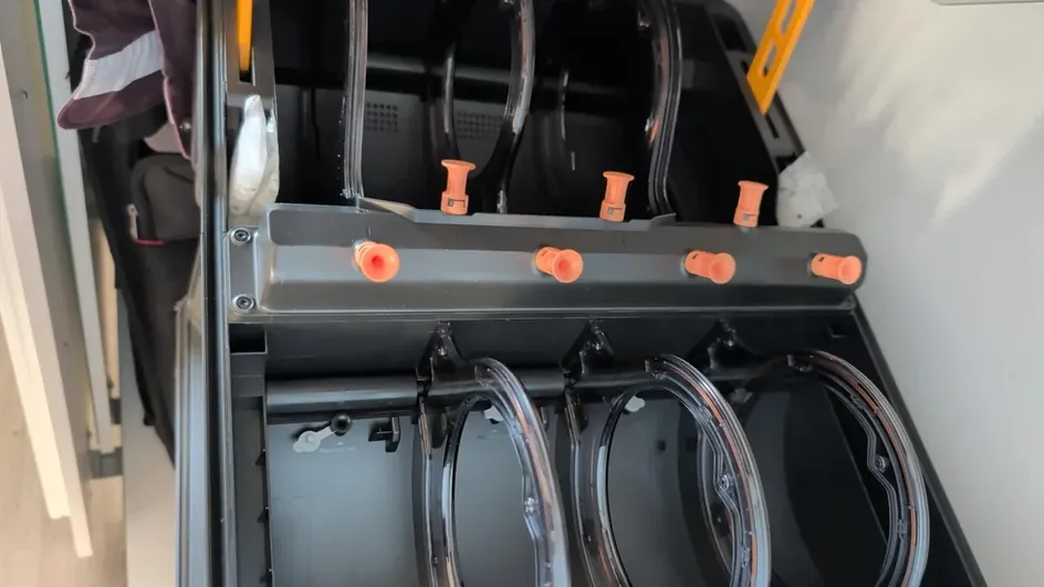 Leaked photo looking down into the Bambu Lab AMS 3P with its lid open, showing clear spool rings and seven orange feeding funnels on a gray center bar